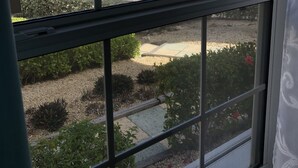 A view through a window of a beachside property with a clear view of the ocean, a sandy beach, and a small building with a blue roof.