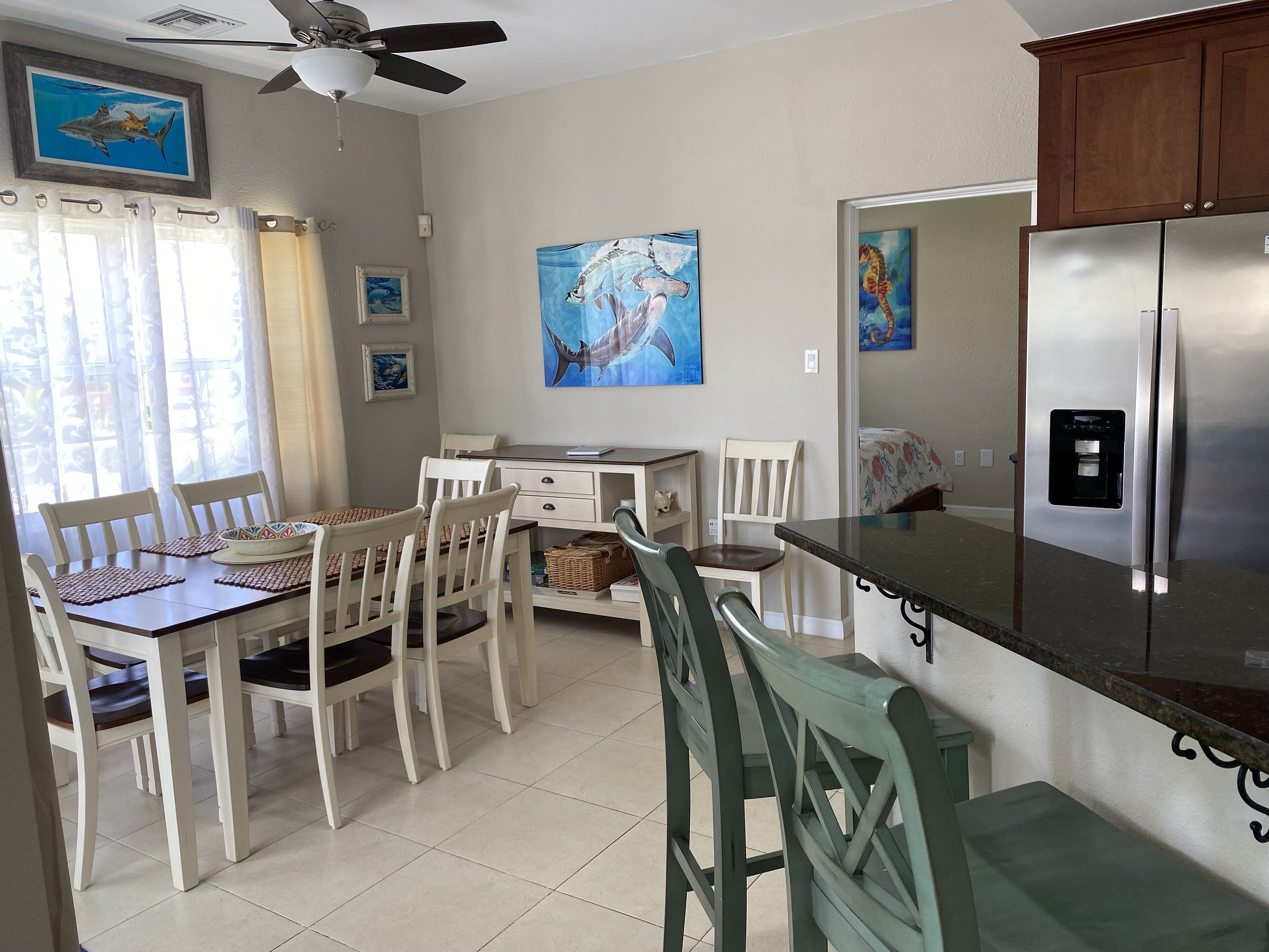 A kitchen with a dining table, chairs, a refrigerator, and artwork on the walls.