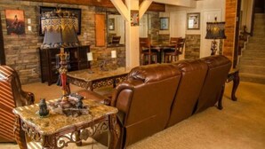A cozy living room with a fireplace, leather sofa, and a dining area with a chandelier. - Raw Hide Lodge - Unit M1 (Ruidoso)