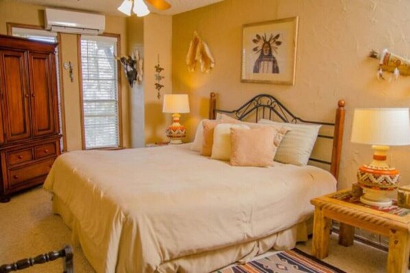 A bedroom with a bed, bedside lamps, a wooden nightstand, and a dresser. - Raw Hide Lodge - Unit M1 (Ruidoso)