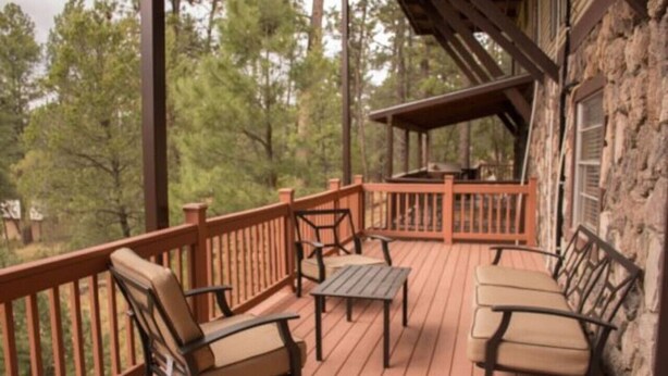 A wooden deck with outdoor furniture, a stone wall, and a view of trees. - Raw Hide Lodge - Unit M1 (Ruidoso)