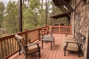 A wooden deck with outdoor furniture, a stone wall, and a view of trees. - Raw Hide Lodge - Unit M1 (Ruidoso)