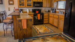 A kitchen with wooden cabinets, a black refrigerator, and a tiled floor. - Raw Hide Lodge - Unit M1 (Ruidoso)