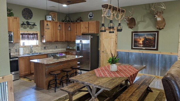 A kitchen with wooden cabinets, a stainless steel refrigerator, and a dining area with a wooden table and benches. - Quiet country getaway located within 10 minutes from town (Pratt)