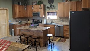A kitchen with wooden cabinets, a central island with stools, a refrigerator, and a microwave. - Quiet country getaway located within 10 minutes from town (Pratt)