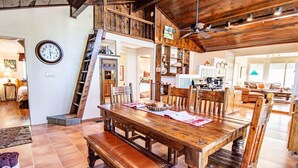 A rustic dining area with a wooden table and benches, a staircase, and a clock on the wall.