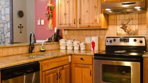 A kitchen with wooden cabinets, a stainless steel dishwasher, and a stove. - Come Stay in Elk Run - I2 (Ruidoso)