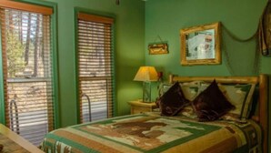 A bedroom with a bed, a nightstand, a lamp, and a window with blinds. - Come Stay in Elk Run - I2 (Ruidoso)