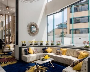 A modern hotel lobby with a seating area, large windows, and a decorative mirror.