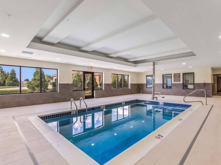Une piscine intérieure avec des parois en verre transparent, un sol carrelé et un plafond doté d’un éclairage encastré.