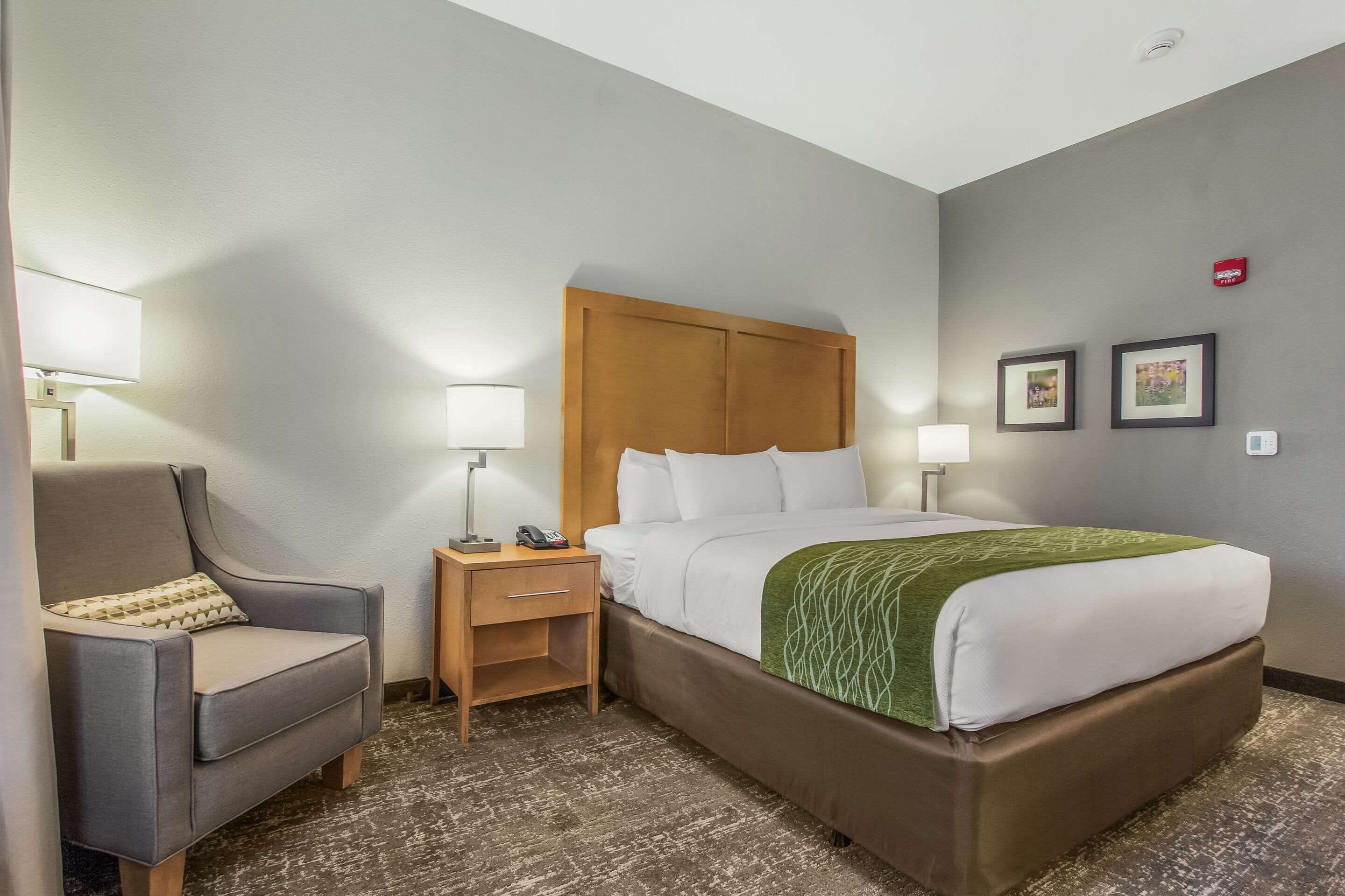 A hotel room with a bed, a chair, a nightstand, and two wall-mounted lamps.