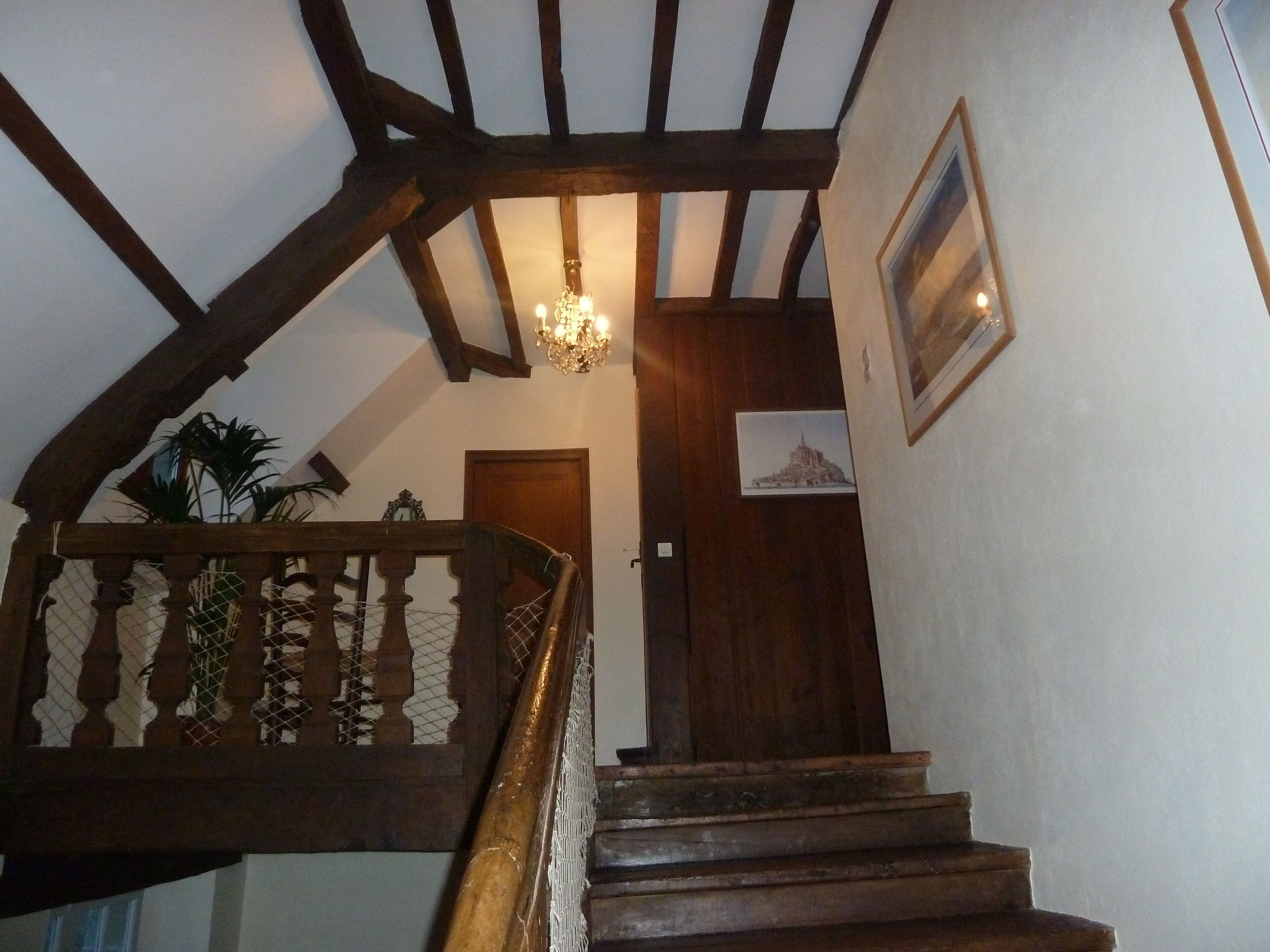 Una escalera de madera con un candelabro, una puerta y un cuadro enmarcado en la pared.