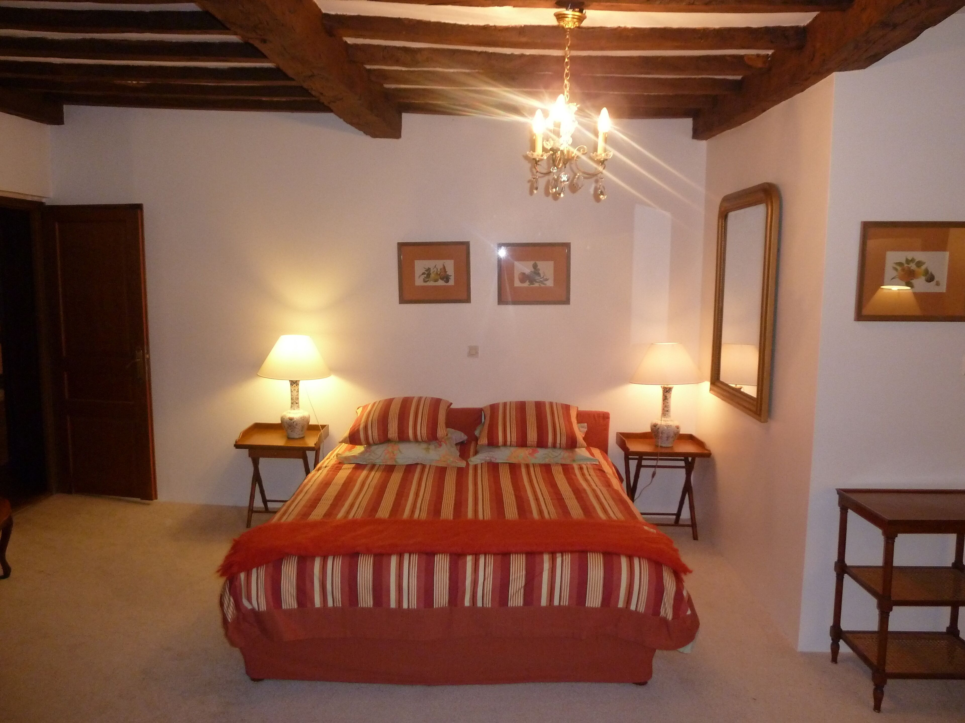 Une chambre à coucher avec un lit, deux tables de chevet avec des lampes, un plafond en bois et deux tableaux encadrés accrochés au mur.