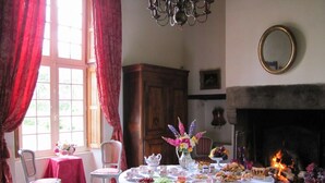 A dining room with a round table set for a meal, a fireplace, and a window with curtains. - Malouinière des Trauchandières Saint-Malo (Saint-Jouan-des-Guerets)