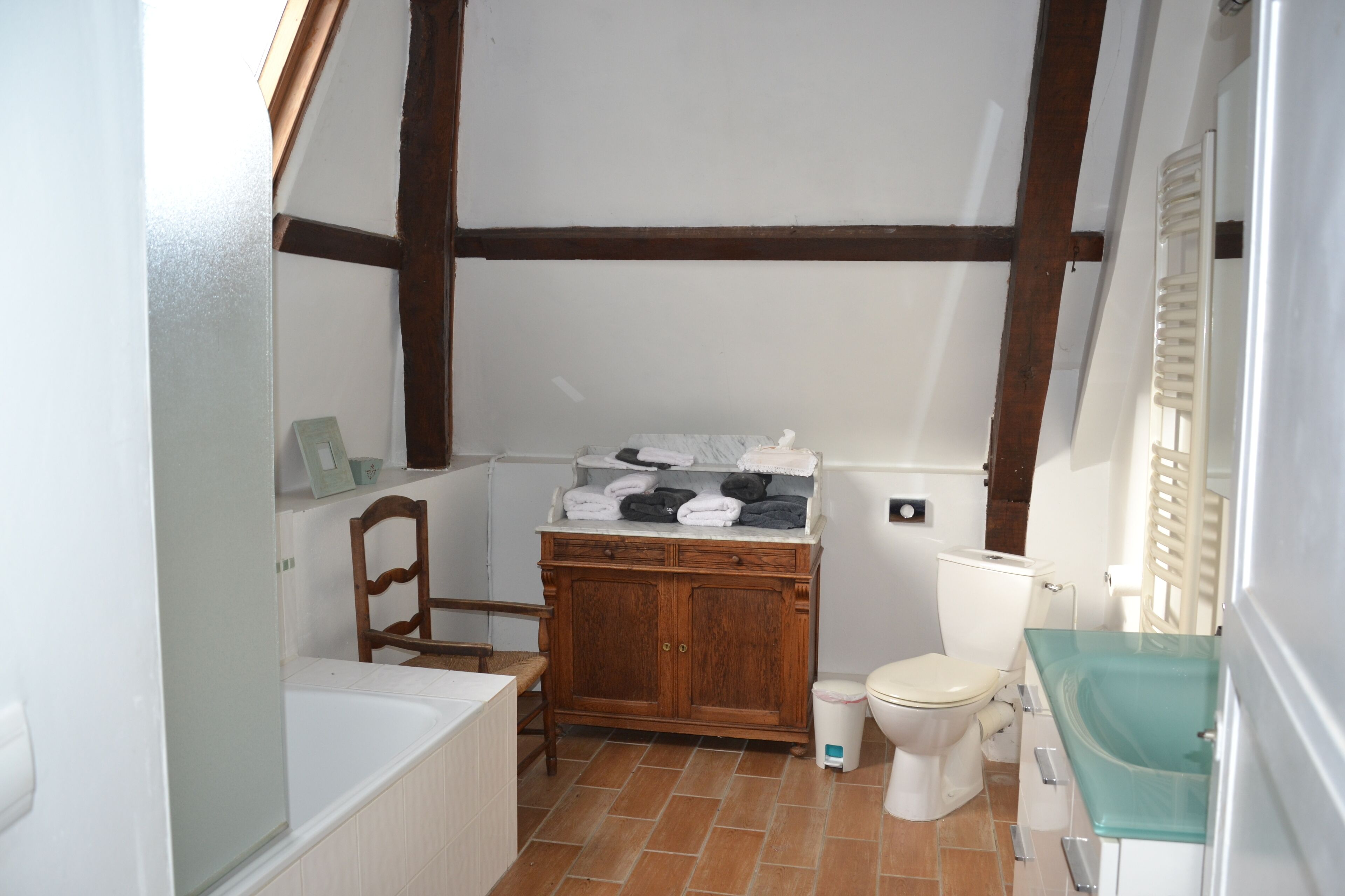 Une salle de bain avec un meuble en bois, des toilettes, une baignoire et un lavabo en verre.