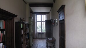 A narrow hallway with wooden bookshelves on one side, a wooden table with a chair, and a large window at the end. - Malouinière des Trauchandières Saint-Malo (Saint-Jouan-des-Guerets)