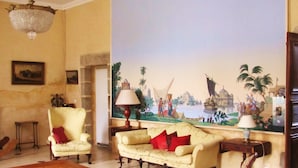 A living room with a large mural, a chandelier, and classic furniture. - Malouinière des Trauchandières Saint-Malo (Saint-Jouan-des-Guerets)