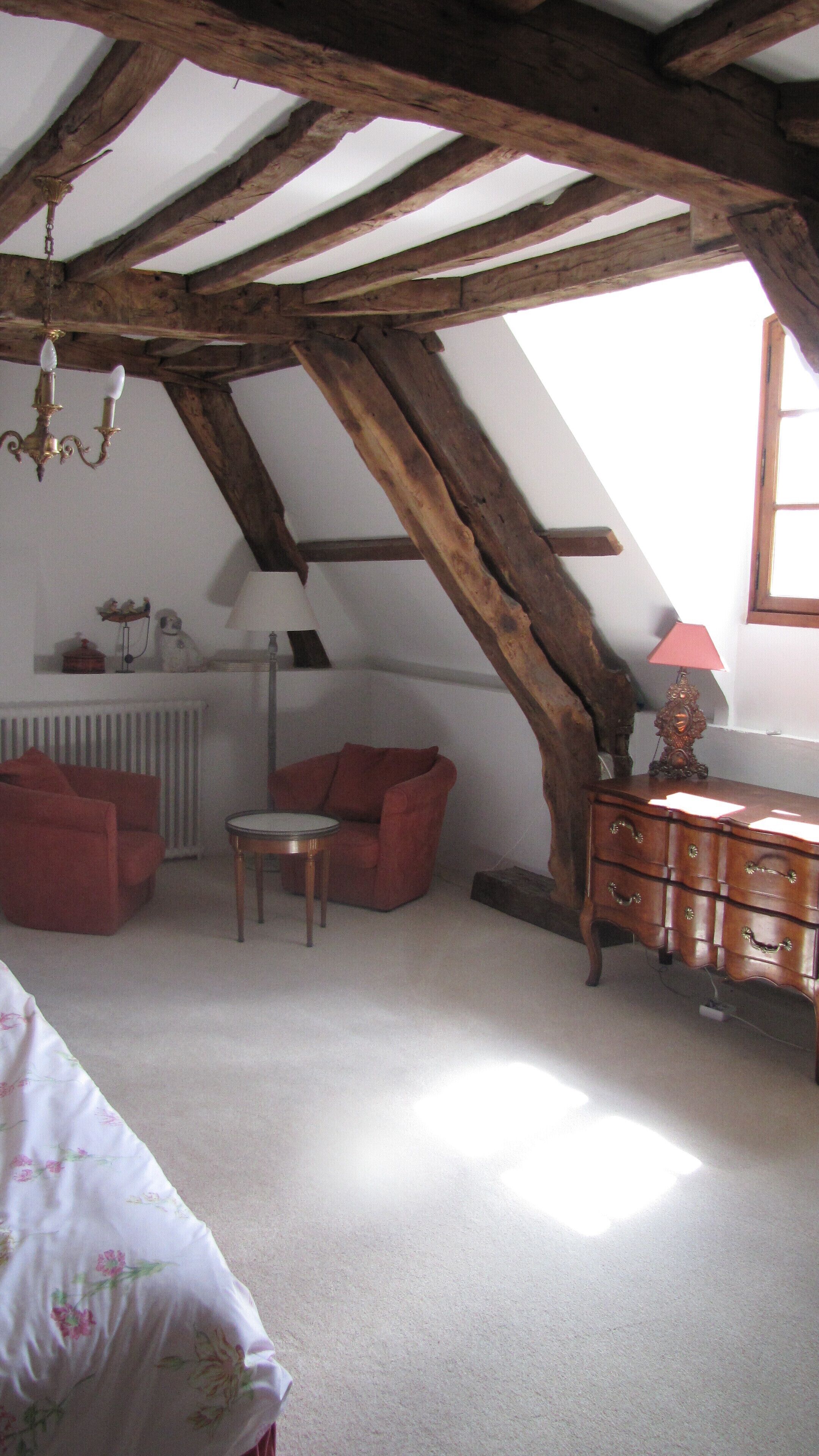 A room with a sloped ceiling, a red armchair, a wooden dresser, and a radiator.