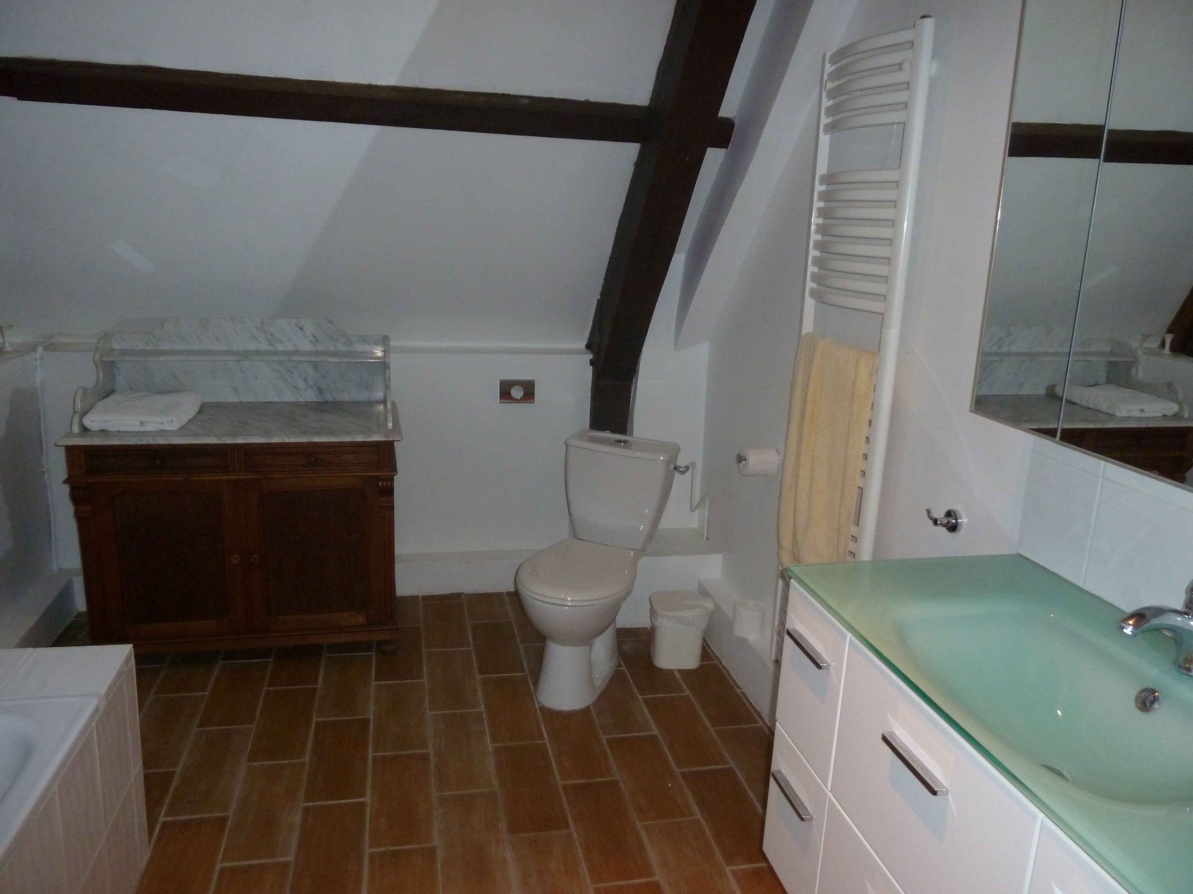 A bathroom with a toilet, a wooden vanity, a marble countertop, a green sink, and a mirror.