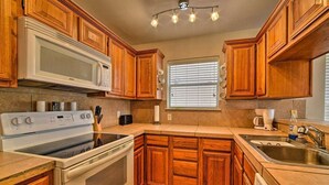 A kitchen with wooden cabinets, a microwave, stove, and a window with blinds.