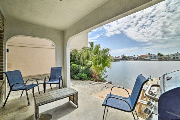 An outdoor patio with a view of a lake, featuring a grill and seating area.