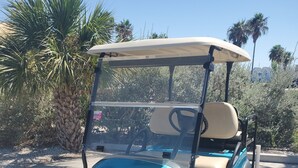 A golf cart parked on a paved area with palm trees and a clear sky in the background.