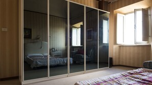A bedroom with a large sliding closet, a bed with a patterned bedspread, and a window with curtains. - The House Of Mario (Monte San Pietrangeli)