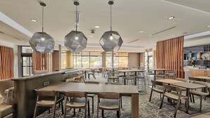 A modern hotel lobby with hexagonal pendant lights, a central bar area, multiple seating arrangements, and large windows offering a view of the outside. - Springhill Suites by Marriott Durango (Durango)