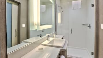 A modern bathroom with two sinks, a large mirror, and a walk-in shower.