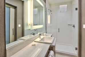 A modern bathroom with two sinks, a large mirror, and a walk-in shower.