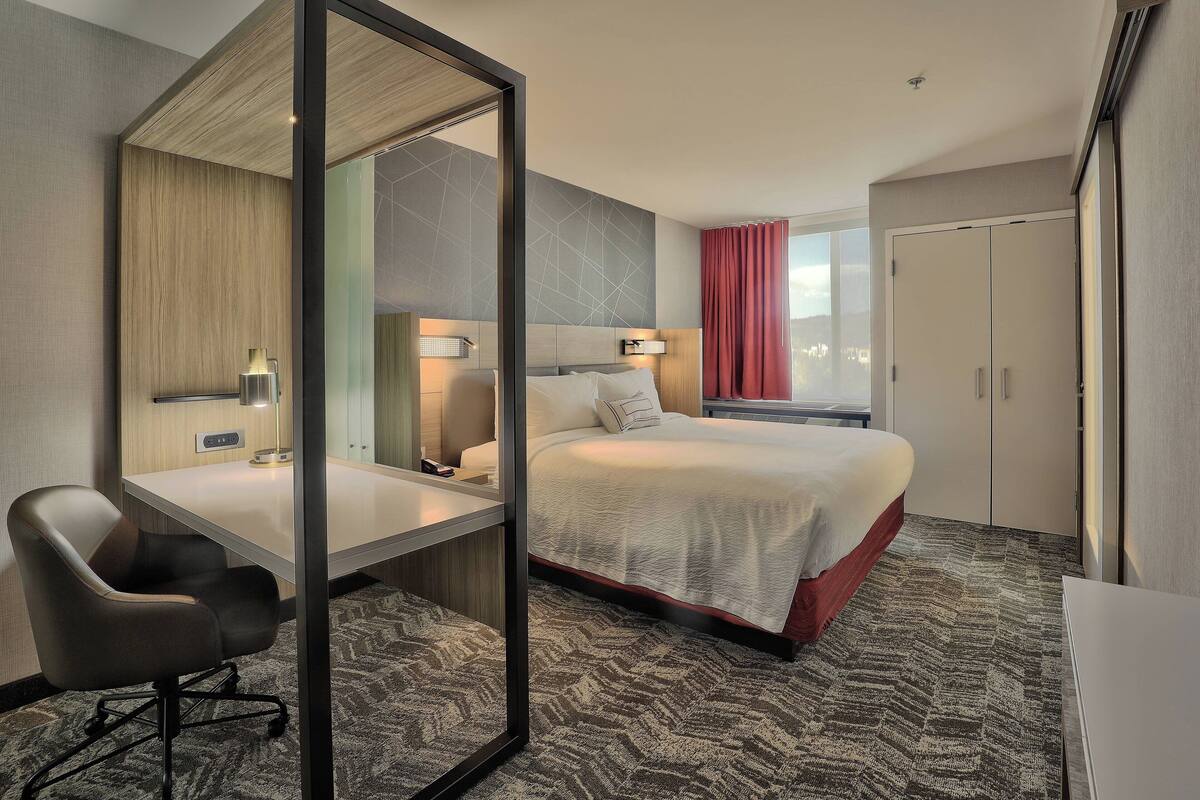 A hotel room with a bed, a desk, a chair, a mirror, and a wardrobe.