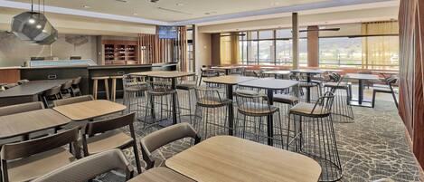 A spacious restaurant with multiple tables and chairs, a counter, and large windows offering a view.