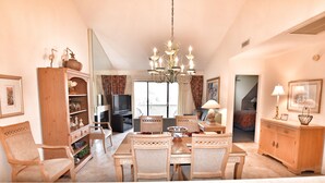 A dining area with a chandelier, wooden chairs, a table, and a television in the background. - Beautiful Lake View Villa in the Prestigious Kingston Plantation/Pools/Lakes (Myrtle Beach)