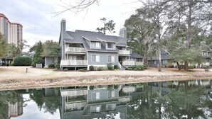 A two-story building with a balcony, located next to a body of water. - Beautiful Lake View Villa in the Prestigious Kingston Plantation/Pools/Lakes (Myrtle Beach)