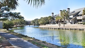 A canal with a wooden bridge, surrounded by residential buildings and palm trees. - Beautiful Lake View Villa in the Prestigious Kingston Plantation/Pools/Lakes (Myrtle Beach)
