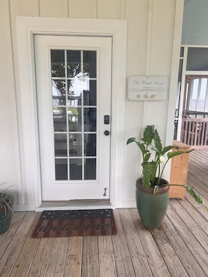 Une porte blanche avec un panneau de verre, une plante en pot, un banc en bois et un panneau indicateur sur le mur.