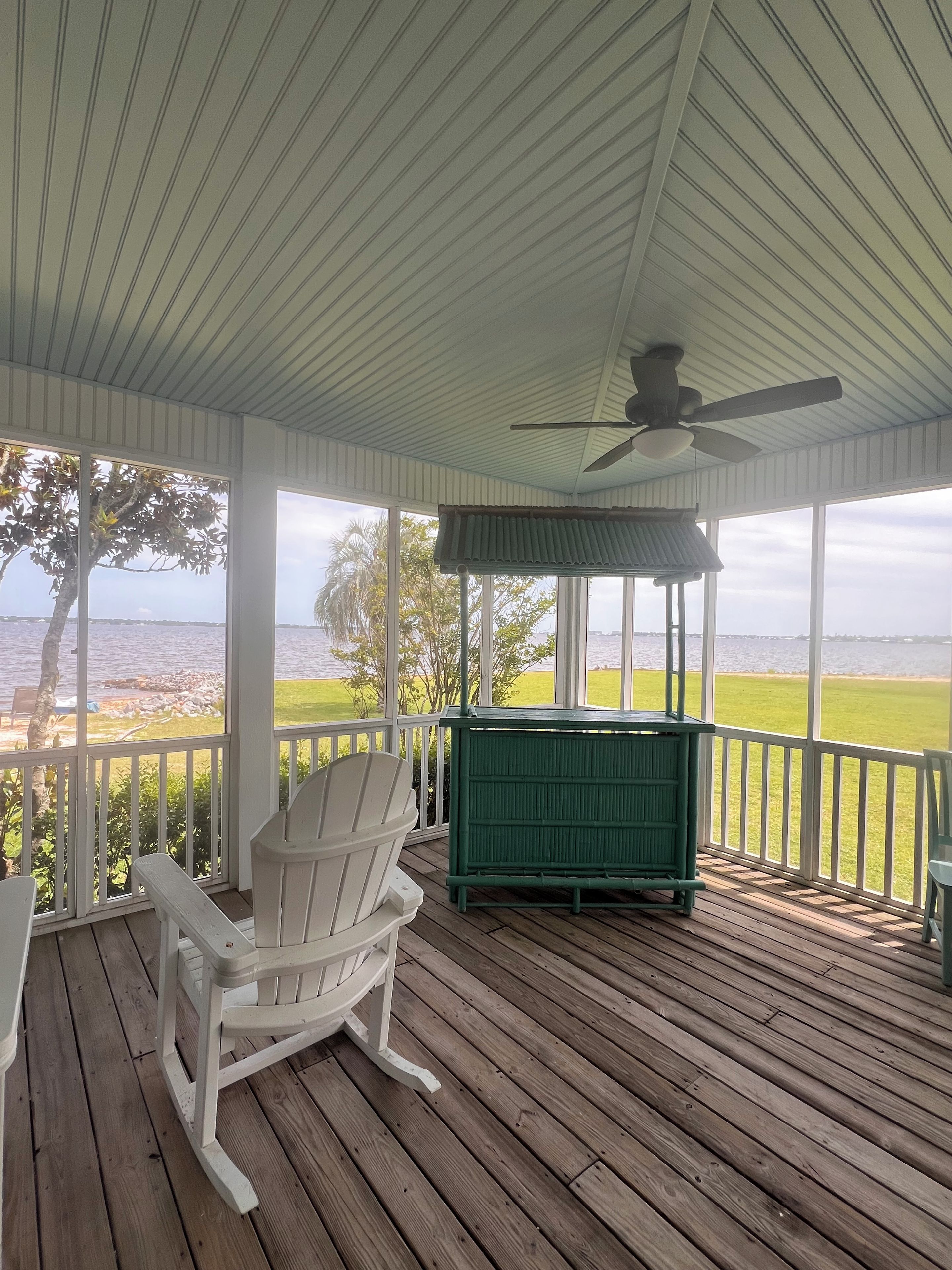 A covered porch with a ceiling fan, a green bench, and a white rocking chair.