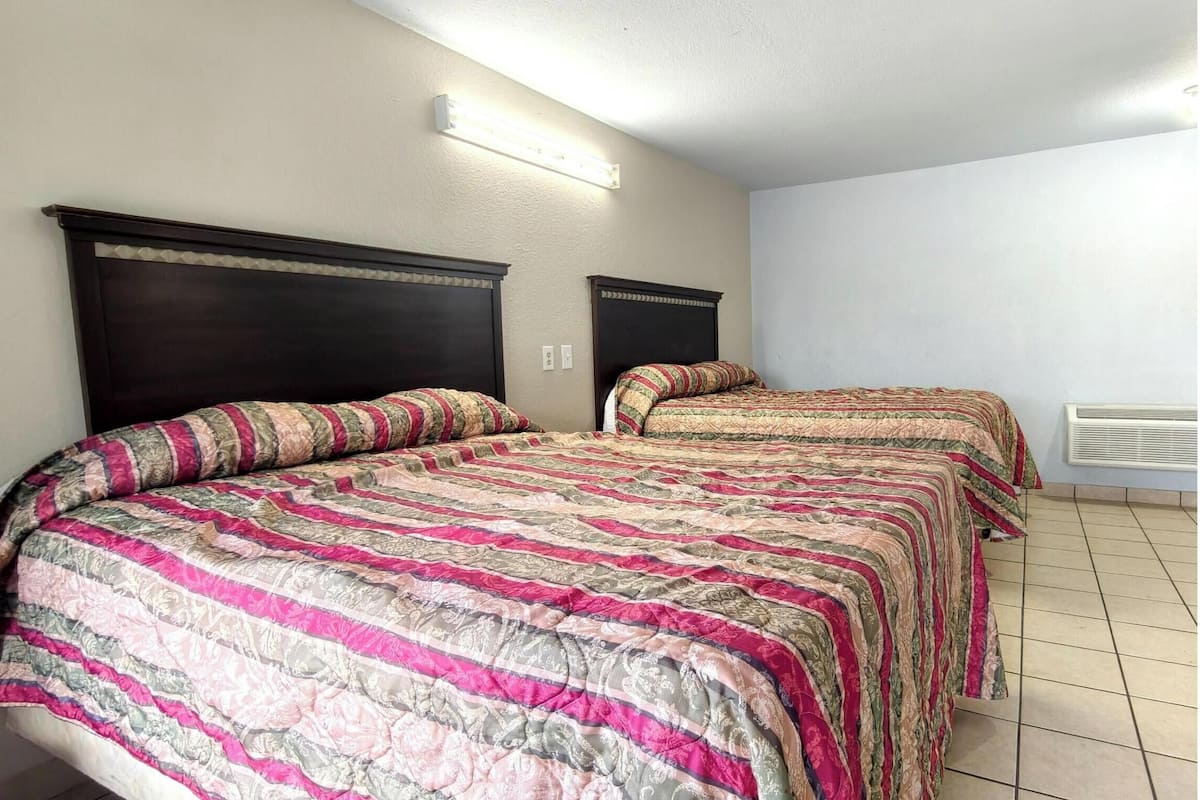A room with two beds, each with a striped bedspread, a light fixture above the beds, and a white wall.