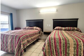 Ein Zimmer mit zwei Betten, einem Fenster mit Vorhängen, einem Nachttisch und einer Wandleuchte.