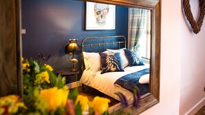 Un dormitorio con cama, mesita de noche, lámpara y espejo que refleja la habitación.