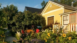 Une maison jaune avec un garage, entourée d’un jardin où poussent des tournesols et d’autres plantes.