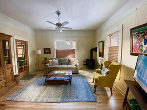 Ein Wohnzimmer mit Deckenventilator, einer Couch, einem gelben Sessel, einem Couchtisch und einem Kamin.
