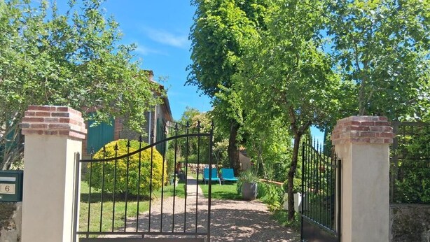 Une entrée fermée par un portail, avec un chemin menant à un espace vert agrémenté d’arbres et d’un banc.
