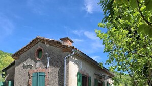 Une maison de campagne en pierre, avec des volets verts, un petit jardin agrémenté d’une piscine et un espace salon extérieur.