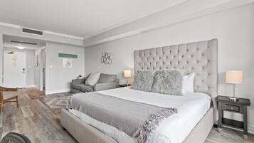 A modern hotel room with a large bed, a grey sofa, a small table, and a wall-mounted artwork.