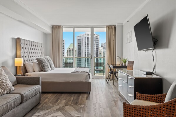 A modern hotel room with a large bed, a sofa, a desk, and a TV.