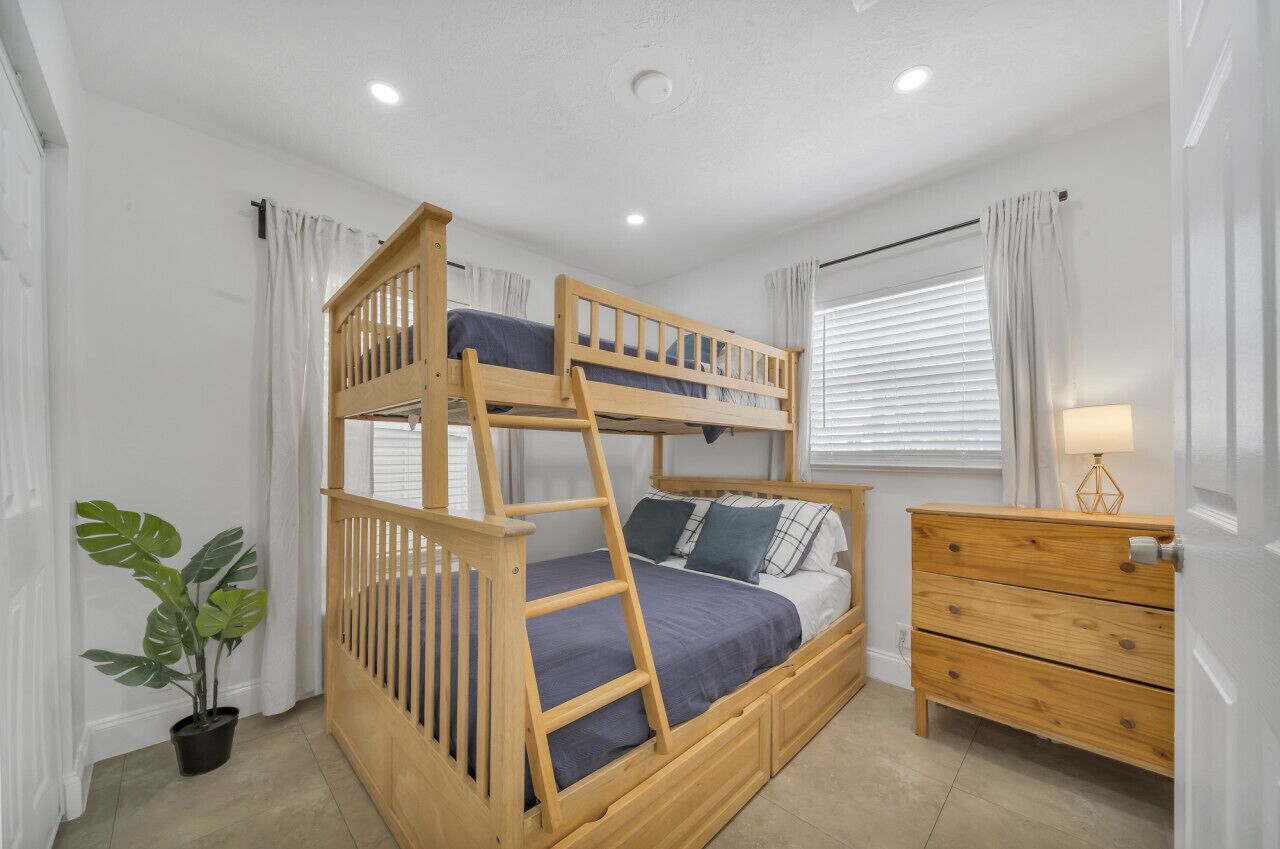 Una cama litera con estructura de madera, una mesita de noche y un aparador.