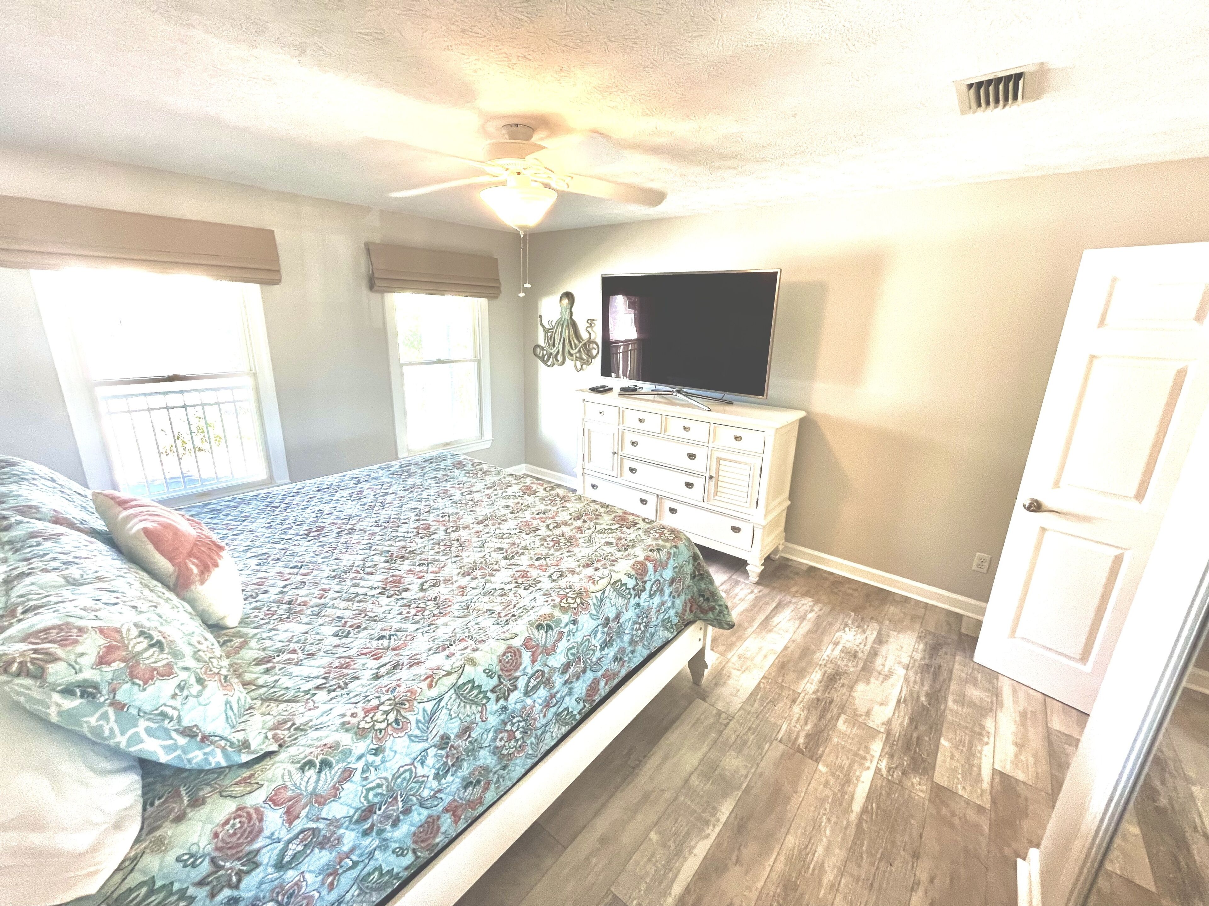 Ein Schlafzimmer mit Bett, Kommode, Deckenventilator und Fernseher.