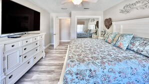 Een slaapkamer met een groot bed, een dressoir, een plafondventilator en een televisie.