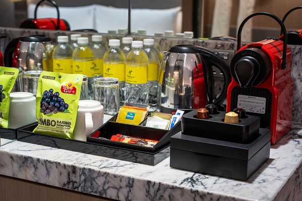 Minibar de una habitación de hotel con diversas bebidas, aperitivos y una máquina de café.